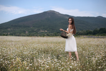 Beautiful girl outdoors with a bouquet of flowers in a field of white daisies,enjoying nature. Beautiful Model with long hair in white dress having fun on summer Field with blooming flowers,Sun Light.