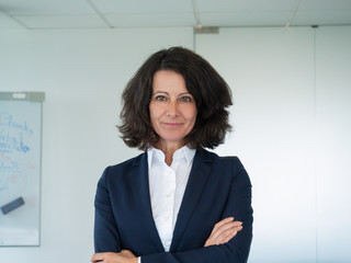 Successful female business trainer posing in boardroom. Businesswoman standing in office with arms...