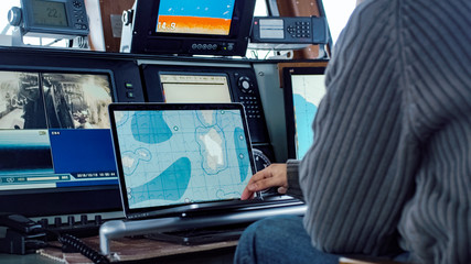 Captain of Commercial Fishing Ship Surrounded by Monitors and Screens Working with Sea Maps in his...