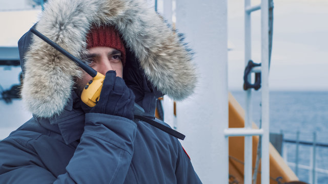 Polar Scientist In Warm Jacket Standing On Ship And Using Radio For Communication. Polar Research Exploration.