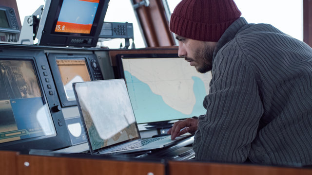 Captain of Commercial Fishing Ship Surrounded by Monitors and Screens Working with Sea Maps in his Cabin.