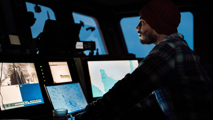 Shot of a Serious Captain on a Commercial Fishing Ship Surrounded by Monitors and Screens Working...