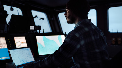 Shot of a Serious Captain on a Commercial Fishing Ship Surrounded by Monitors and Screens Working with Sea Maps Pilots.