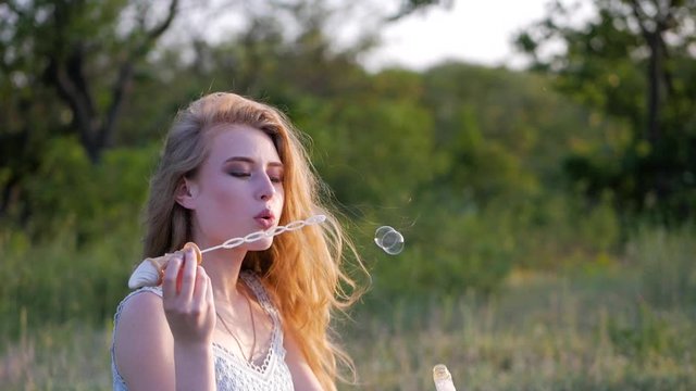 Young pretty woman on a green meadow blowing bubbles