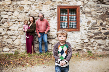 A small boy with his family standing in front of old stone house.