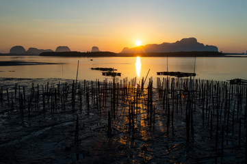 Fishermen village at sunrise..Silhouette landscape of fishermen floating basket and bamboo rods when the sun is coming up from the mountain with golden water reflection and twilight clear sky.
