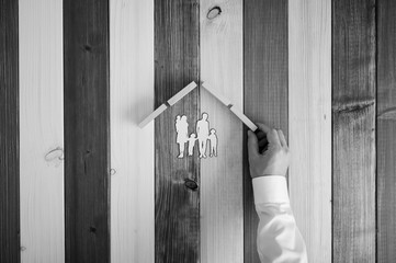 Male hand making a roof over paper cut family shape