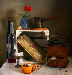 Still life with a cup of aromatic coffee, a coffee grinder, wine, an old cookbook and a flower. Vintage.
