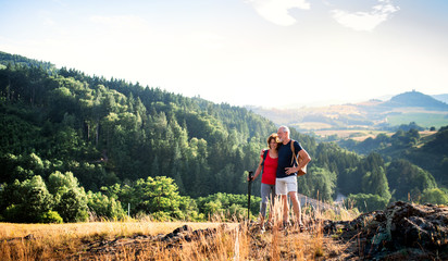 Senior tourist couple with backpacks hiking in nature, resting.