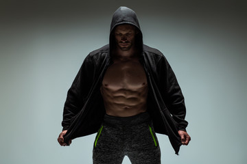 Strong young man with muscular body in black sport jacket with hood. 