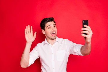 Photo of handsome trendy man speaking with friends by recording videos with telephone of his while isolated with red background
