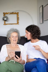 Senior and middle aged women using smartphone. Senior mother with adult daughter sitting together on couch and using mobile phone. Technology concept