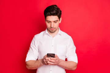 Photo of serious man searching for something on internet by browsing through telephone while isolated with red background