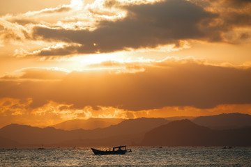 Naklejka na ściany i meble Lonely boat in the ocean by unset with mountains in the horizon. Sunset Over Lombok Island, Indonesia