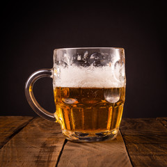 Very cold beer jug on a wooden table on a black background. Concept for the oktoberfest party.