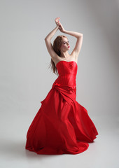 Naklejka premium full length portrait of a girl wearing a long red silk gown, Standing pose on a grey studio background.