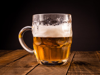 Very cold beer jug on a wooden table on a black background. Concept for the oktoberfest party.