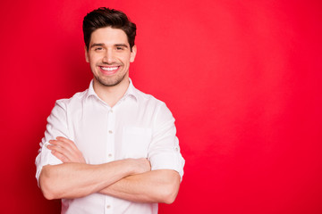 Portrait of cheerful guy with his hands folded smiling wearing white shirt isolated over red background