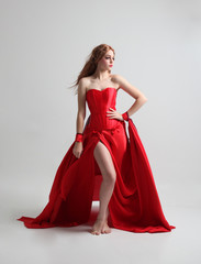 full length portrait of a  girl wearing a long red silk gown, Standing pose on a grey studio background.