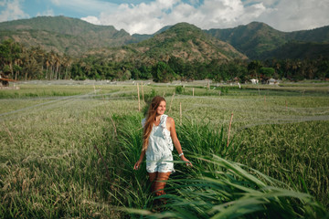 Fototapeta na wymiar Relaxed healthy woman enjoying in pure nature at beautiful green rice fields on Bali. Concept of traveling, healthy and clean environment, ecology, balance in life, freedom, happiness, and well being