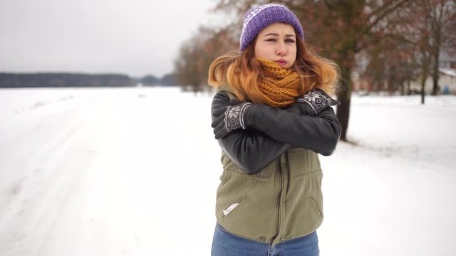 Beautiful girl freezes in the street. A girl in a hat with earflaps is on the street in winter. Russian beauty in a hat with earflaps.