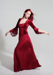 full length portrait of a  girl wearing a  red medieval fantasy gown, Standing pose on a grey studio background.