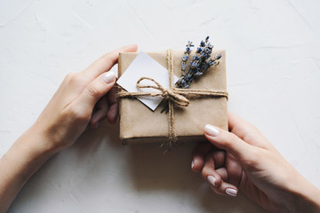 A gift box in a simple concise paper package with a card and a bouquet of lavender in hands with a...