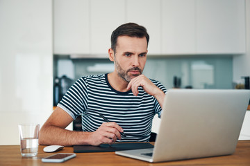 Thoughtful graphic designer working from home with graphics tablet and laptop