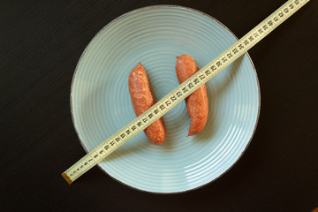 Diet conept - sausages on the plate wrapped with yellow measuring tape