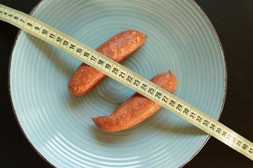 Diet conept - sausages on the plate wrapped with yellow measuring tape