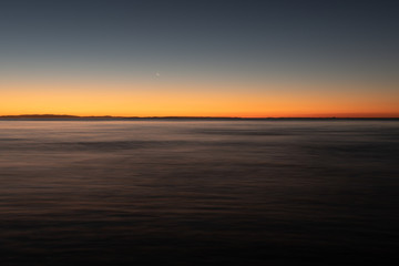 A long exposure captures the crescent moon overlooking over the beautiful gradient created by the sun after it has set into the horizon on North Stradbroke Island, Queensland, Australia