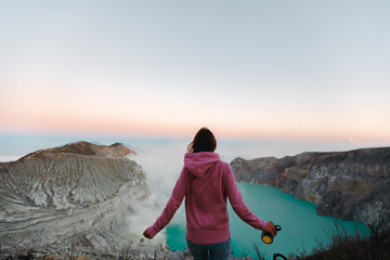Woman standing on edge of crater Kawah Ijen volcano, East Java, Indonesia and holding respirator in hands