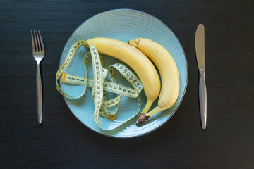Diet concept - bananas on plate with yellow measuring tape