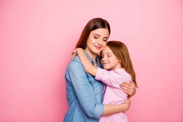 Portrait of relaxed lady hugging her daughter closing eyes wearing denim jeans shirt isolated over...