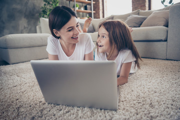 Close up photo of cute student little kid lying on floor watch netbook laughing wearing white t-shirt indoors