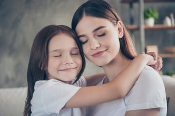 Close up photo of charming student and kid with foxy ginger hair hugging closing eyes wearing white t-shirt in room house indoors