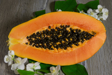 Fresh sliced papaya with seeds inside on a wooden background with jasmine flowers. Half of yellow papaya
