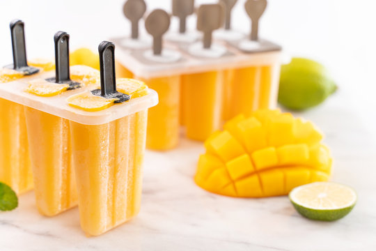 Fresh mango fruit popsicle ice in the plastic shaping box on bright marble table. Summer mood concept product design, close up.