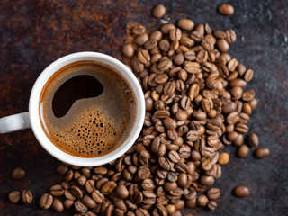 A Cup of espresso on a rusty background with scattered roasted coffee beans . copy space