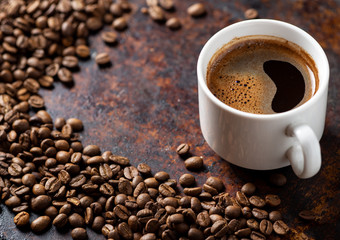A Cup of espresso on a rusty background with scattered roasted coffee beans . copy space