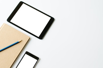 White office desk table with tablet, pencil, sartphone and notebook. Top view with copy space.