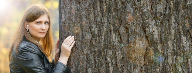 Banner. Cute red-haired girl in white headphones looking at a tree in the woods. Girl with...