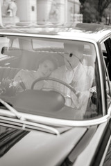 Pretty bride and handsome groom in the retro car. Bride puts her head on the shoulder of groom while they sit together inside a retro car