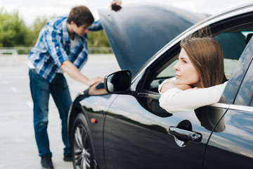 Woman sitting in car while man checks engine