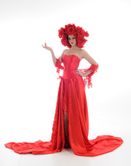 full length portrait of girl wearing long red silk gown and flower headdress. standing pose on white studio background.