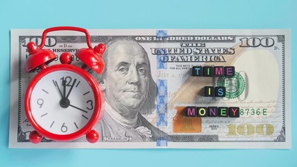 Multicolor text Time ia money and red alarm clock walking ticking on background of American hundreds dollar bills, closeup. Concept, Timelapse. Top view. - Powered by Adobe