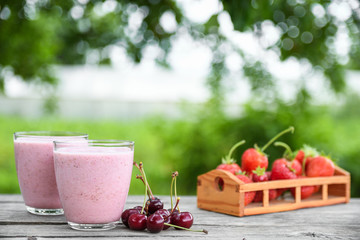 A glass of fresh cold smoothie with berries and cherrys on a wooden table, summer set, outdoor greed blured background,boke.