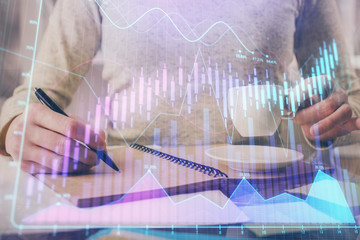 Forex chart hologram on hand taking notes background. Concept of analysis. Double exposure