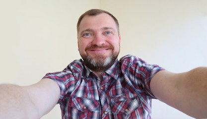 Selfie portrait! Handsome bearded man taking selfie photo and smiling on the light background.