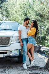 handsome man hugging sexy woman near auto in woods